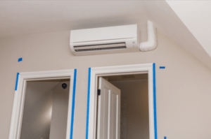 A new ductless mini split unit located at the top of a wall close to a ceiling. It is situated above two doors.