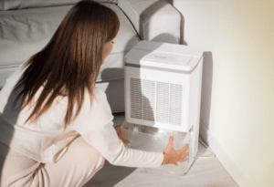 A woman kneeling in front of a dehumidifier.